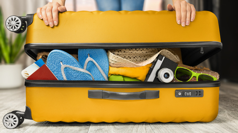 A person trying to close an overstuff piece of luggage