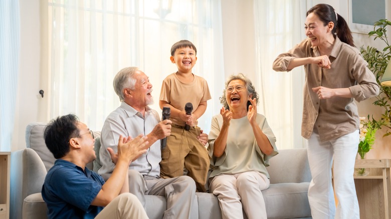 Happy Asian three generation family have fun singing and dancing together in living room.
