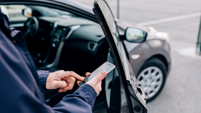A person using a phone outside a car.