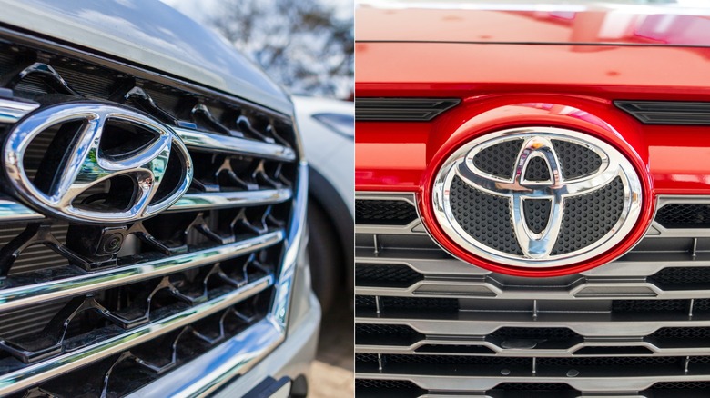 Close-up comparison of Hyundai and Toyota emblems mounted on the front grilles of a silver vehicle and a red vehicle