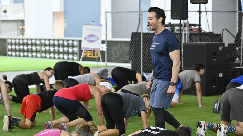 Man leads an outdoor fitness class with participants on hands and knees