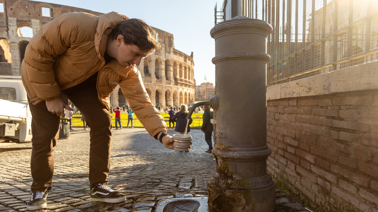 A tourist fills a cup at a drinking fountain in Italy