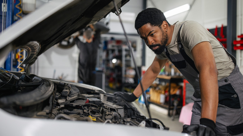 A mechanic leans over the open hood of a car in a shop