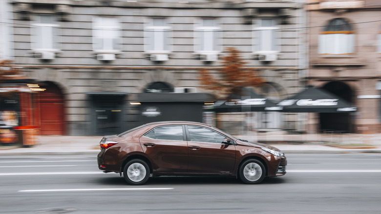 A brown Toyota Corolla car driving down the street