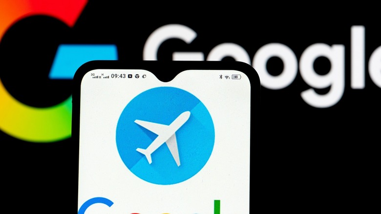 Smartphone displaying the Google Flights app icon with a blurred Google logo in the background