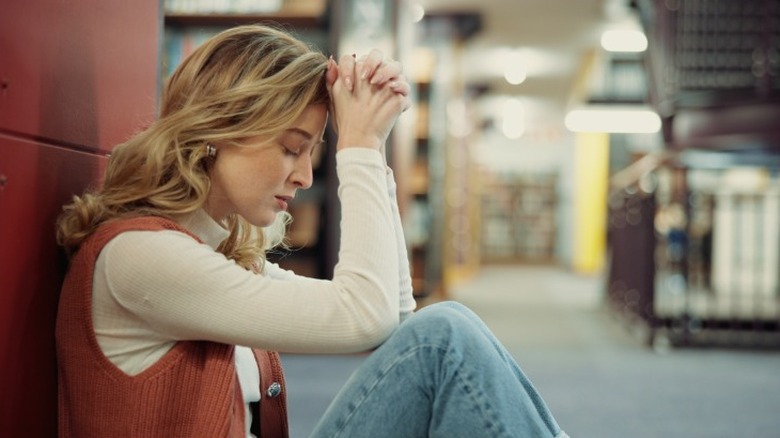 A woman looking stressed sitting against a wall with her elbows on her knees and hands at her forehead.