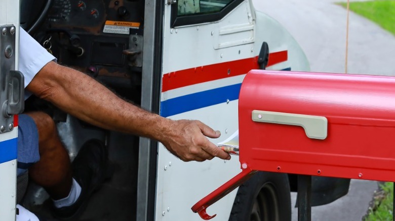 A mail carrier putting mail into a roadside red mailbox straight from his postal service truck.
