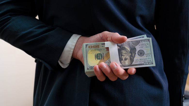 person wearing a dark suit hiding money behind back