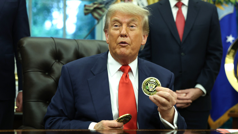 President Donald Trump holds presidential coins in the Oval Office