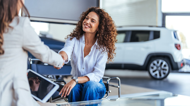 Happy woman shaking hands in a car dealership