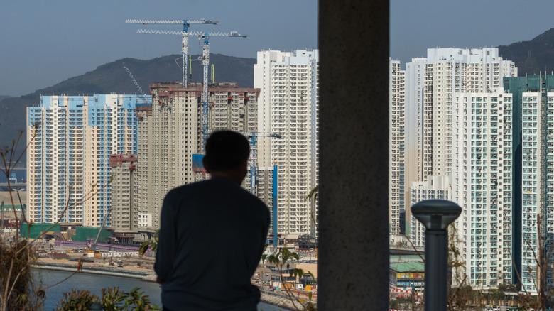 A man in a tall building looking across a river at high rise buildings being built in Hong Kong