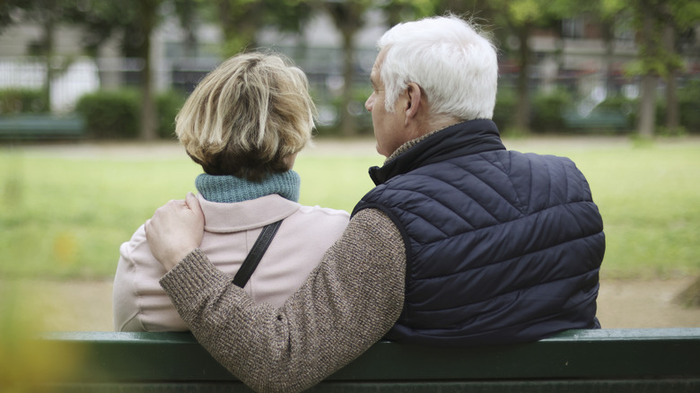 Senior couple on green park bench with backs turned