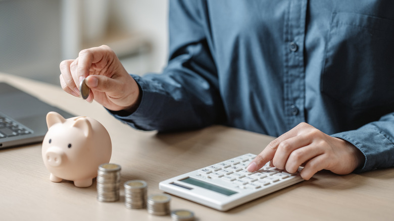 Person calculating savings next to a piggy bank and stacks of coins
