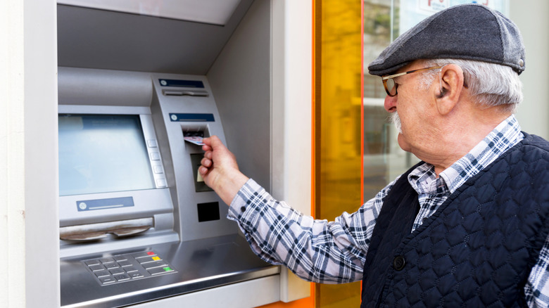 An older man is removing a card from an outdoor ATM.