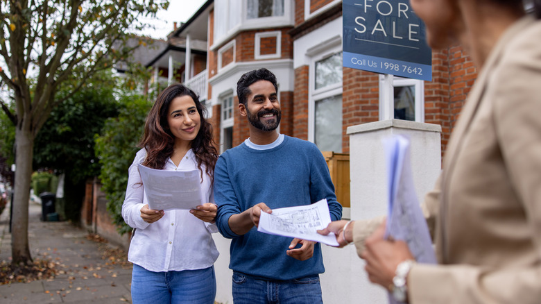 A couple talking to a realtor in front of fore-sale sign on house