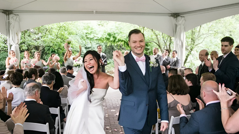 A happy bride and groom walking together down the aisle while guests applaud.