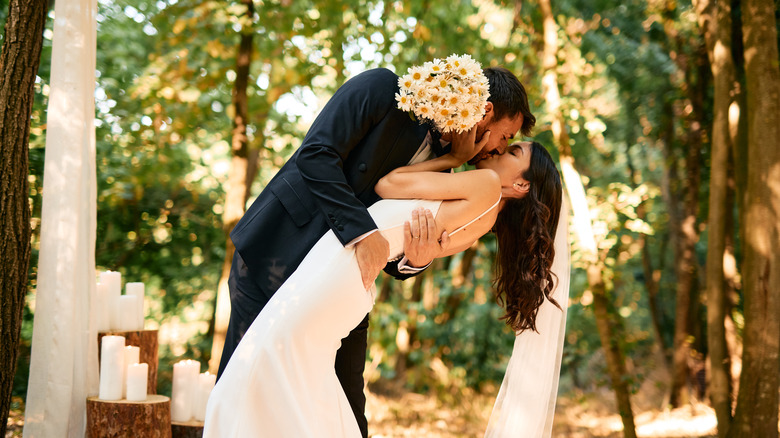 A newlywed bride and groom sharing a kiss in a wooded area.