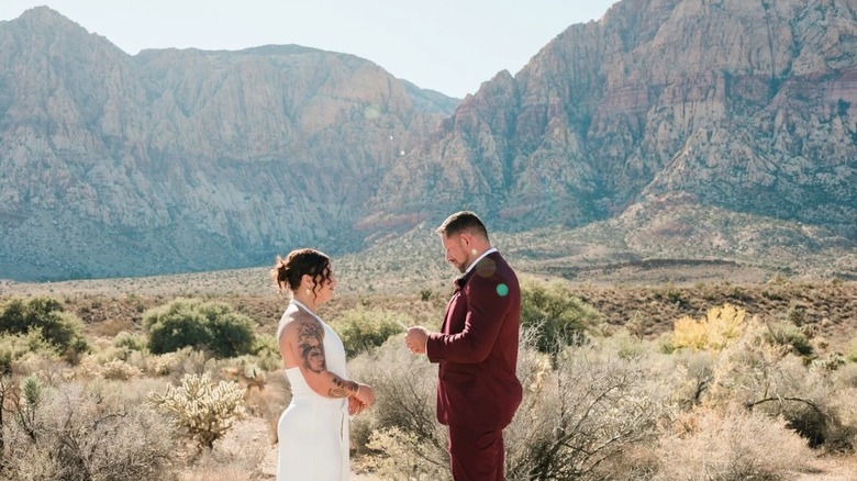 A groom standing in front of his bride with mountains in the background.