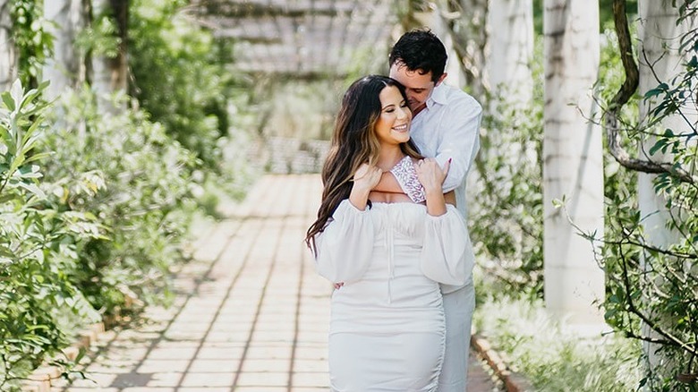 A man and woman dressed in white embracing on a cobblestone pathway.