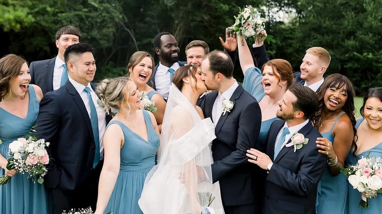 An ecstatic wedding party celebrating around a kissing married couple.