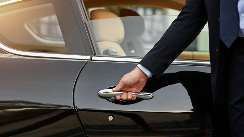 Person in suit opening door to sleek black vehicle