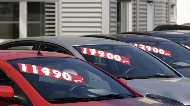 A row of used cars on a dealership lot with prices below $15,000 posted on stickers in their windshields.