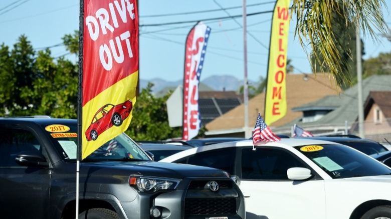 Vehicles sitting in a used car sales lot with feather flags and banners advertising deals.