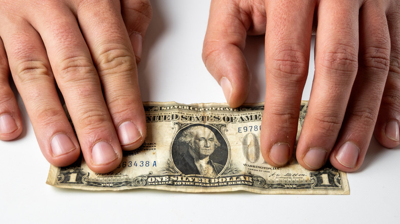 Hands stretching out a well-worn $1 bill across white table