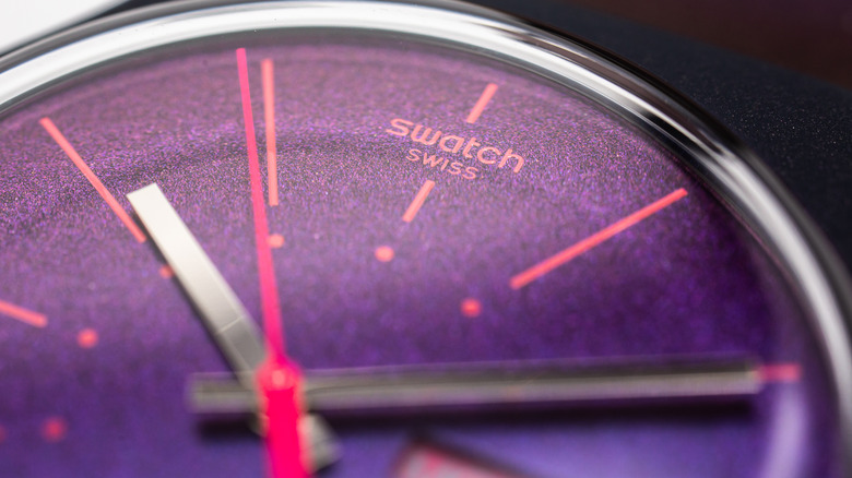An extreme close-up on a colorful pink-and-black speckled Swatch watch face with hot pink hands.