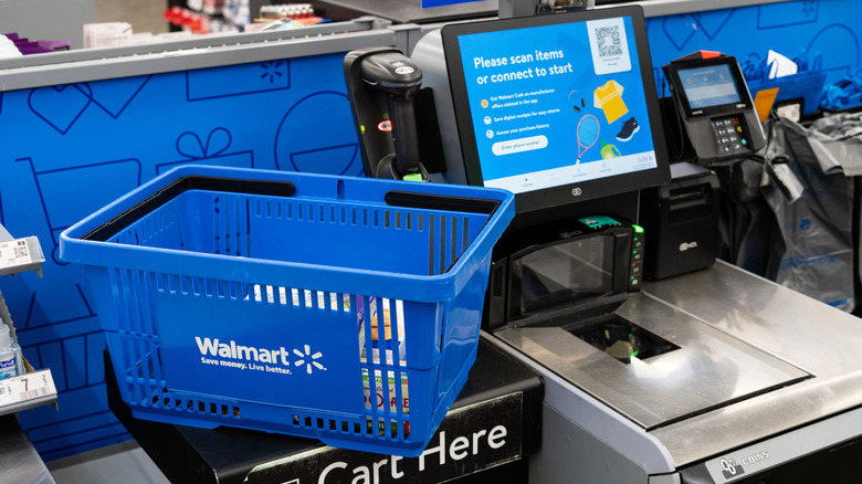A self-checkout register at Walmart with a blue hand basket next to it.