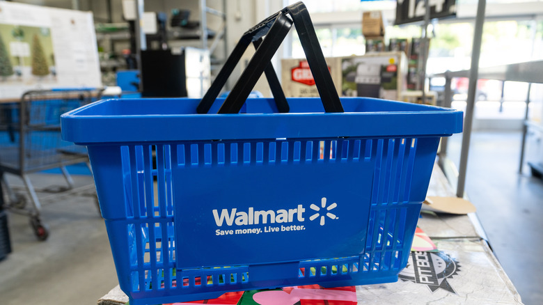 A blue Walmart hand basket with black handles sitting on a table in the store.