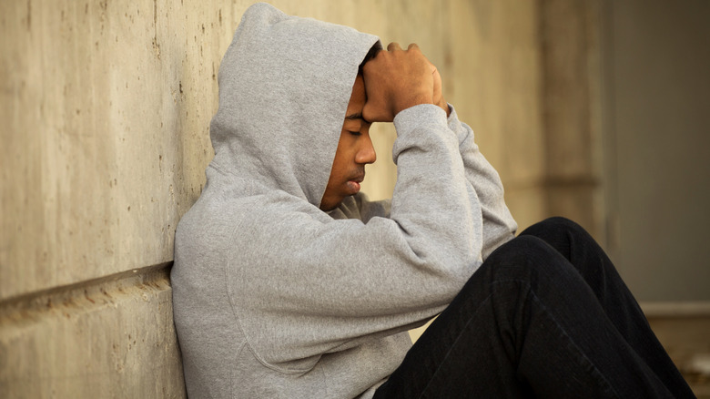 An upset teenager sitting on the ground outside