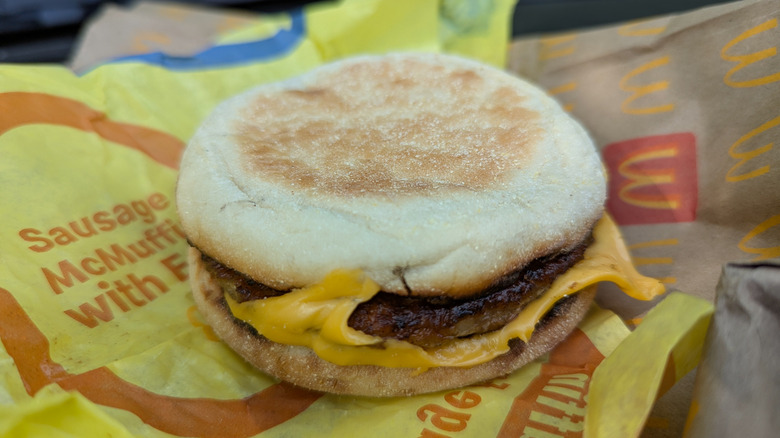 A sausage McMuffin sitting on top of a yellow rapper and a McDonald's bag