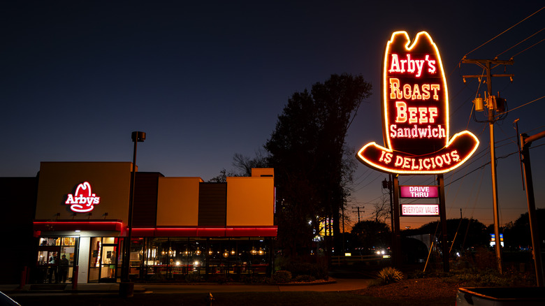 Arby's at dusk, with a brightly illuminated neon sign in the shape of a cowboy hat
