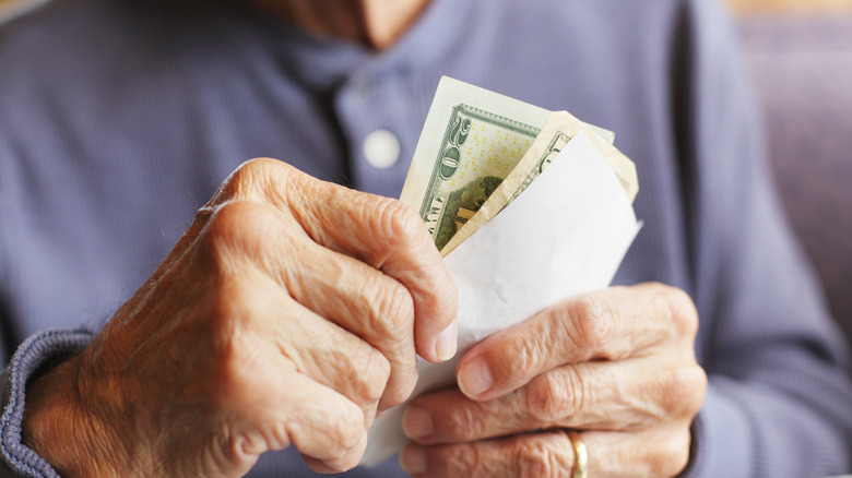 Hands of senior mature man holding ten and twenty dollar bills and a receipt-sized piece of paper