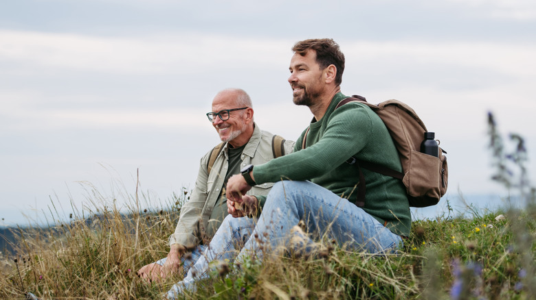 father and son sit on hill, resting from hiking