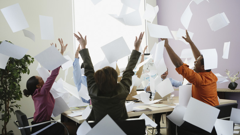 business colleagues at a table tossing paper into the air