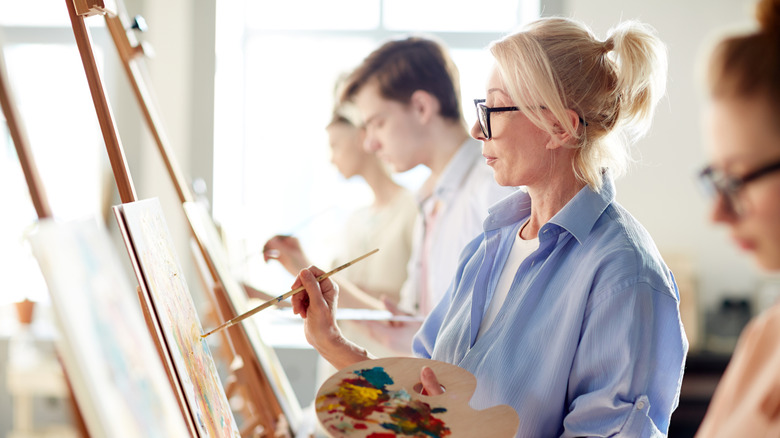 middle-aged woman standing at her easel paints in art class