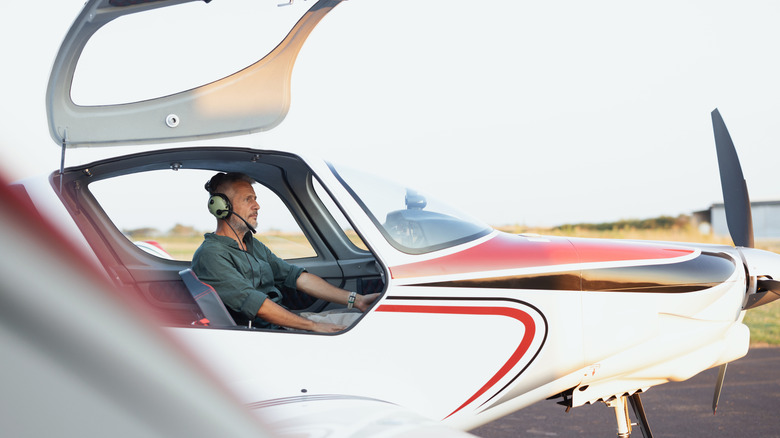 pilot sitting in private single-prop plane on ground with cockpit door open