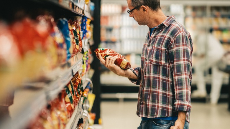 A man examines a bag of packaged food while shopping in a grocery store aisle