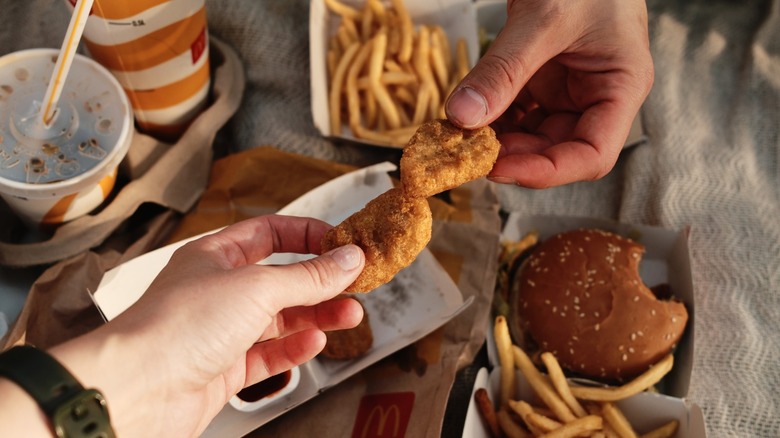 Two people holding up chicken nuggets from McDonald's in a cheers motion over other McDonald's food.