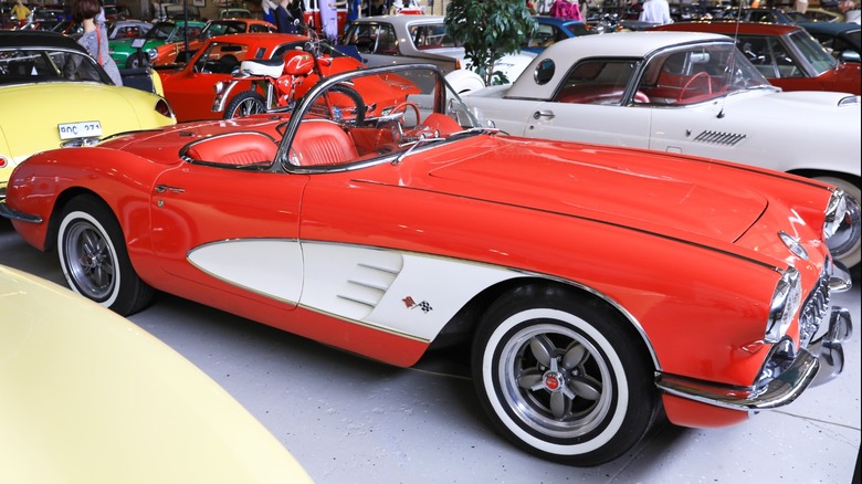 Red-and-white 1960s Chevrolet Corvette convertible displayed indoors at a classic car museum, surrounded by other vintage cars and motorcycles
