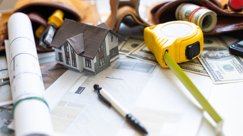 Blueprints, tools, and money laid out on a table.