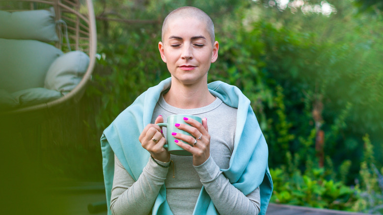 oung female cancer patient sitting on garden patio with coffee, eyes closed.