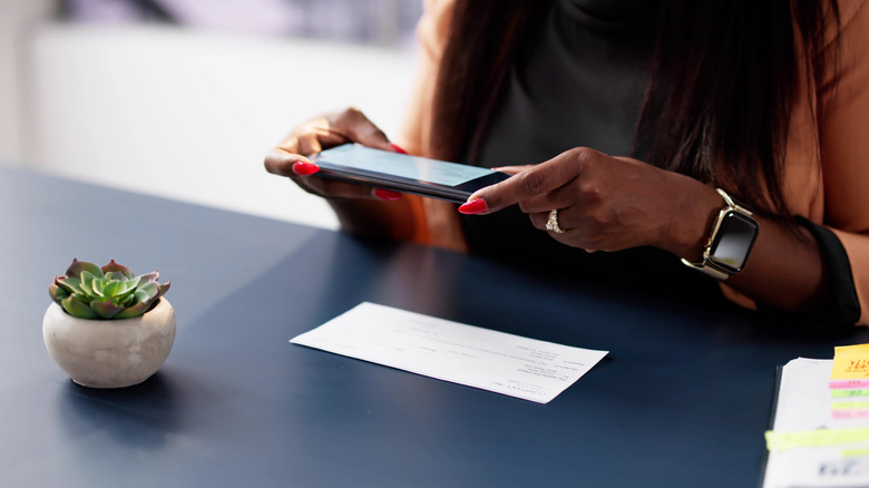 Young woman taking a picture of a check with her phone for a mobile deposit