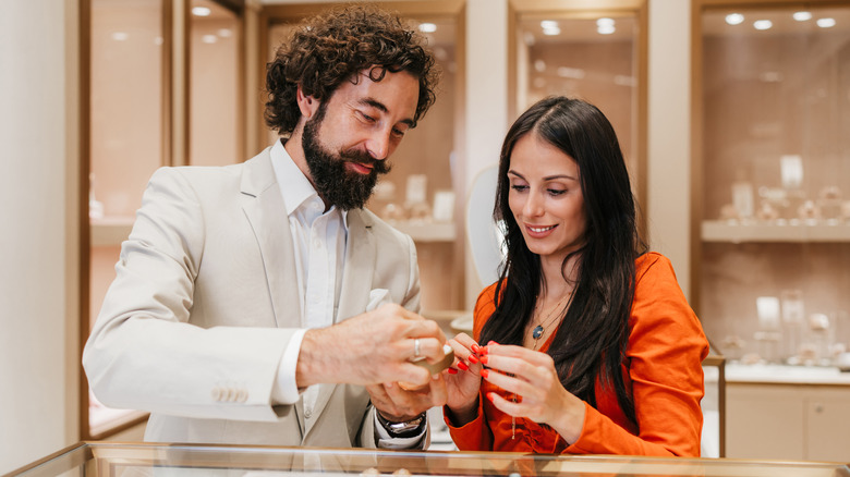 A man shows off a ring to a woman in front of a glass display case