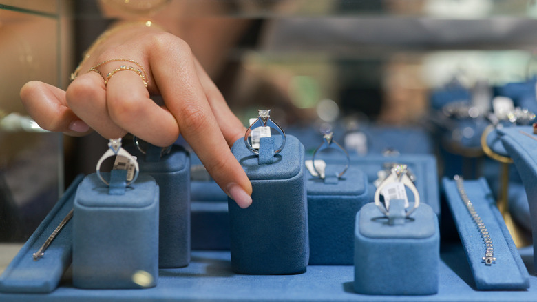 Woman's hand lifts and examines a ring inside a glass display case