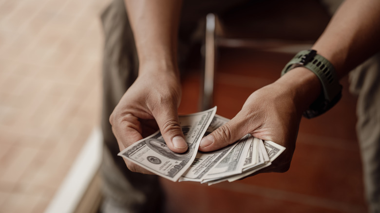 Two hands holding out a fan of $100 bills