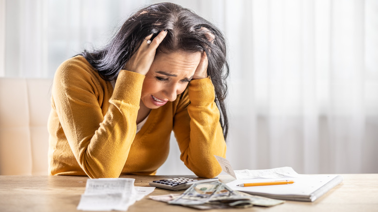 Stressed out woman reviewing finances at table with cash, notepad, and calculator