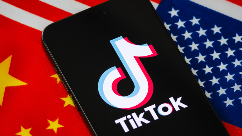 A mobile phone with a TikTok logo against a Chinese flag and American flag